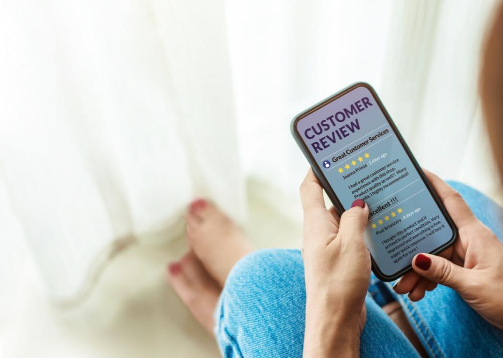 A woman holds her cell phone while reading customer reviews of a new product.